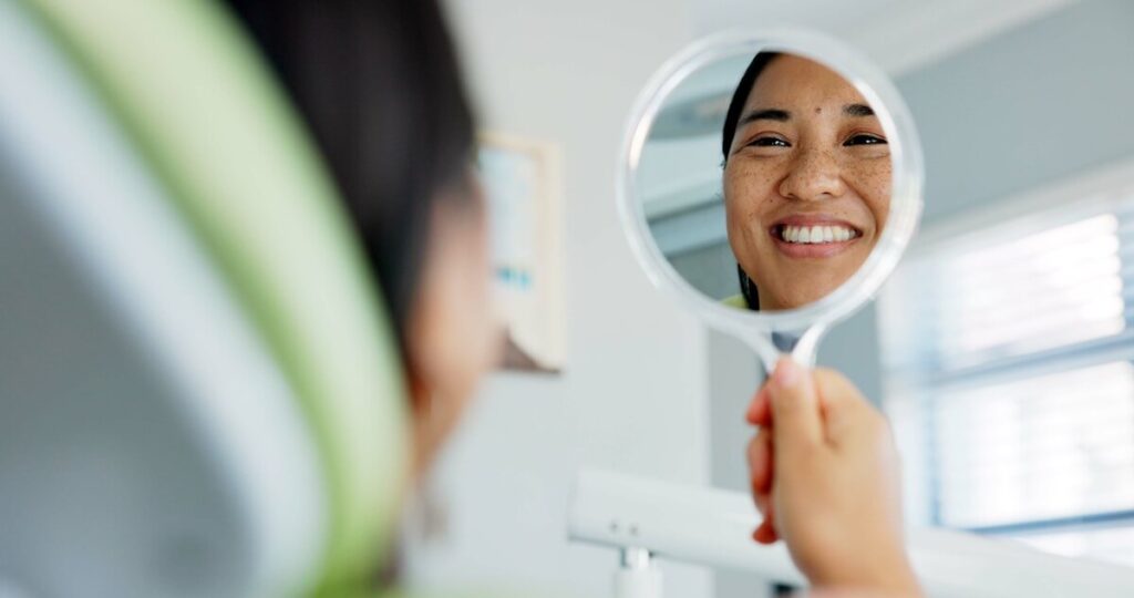 Happy patient checking smile in mirror after treatment