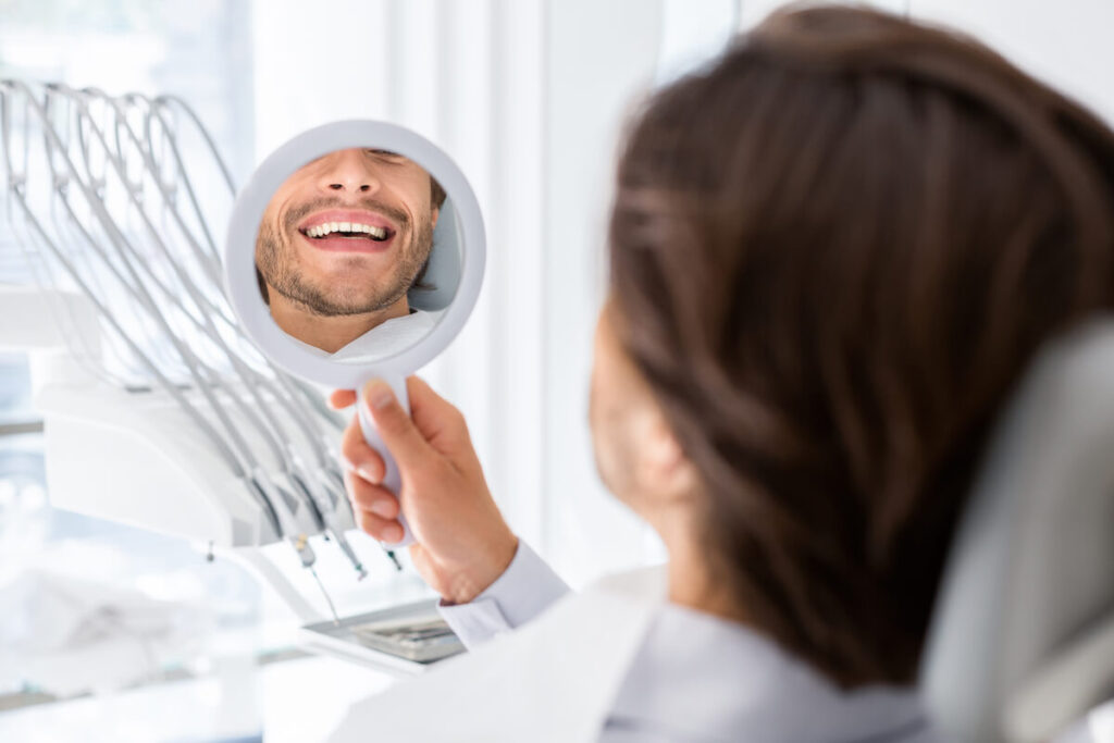 Satisfied patient checking smile at mirror in dent - Oral Plastic Surgery & Periodontics